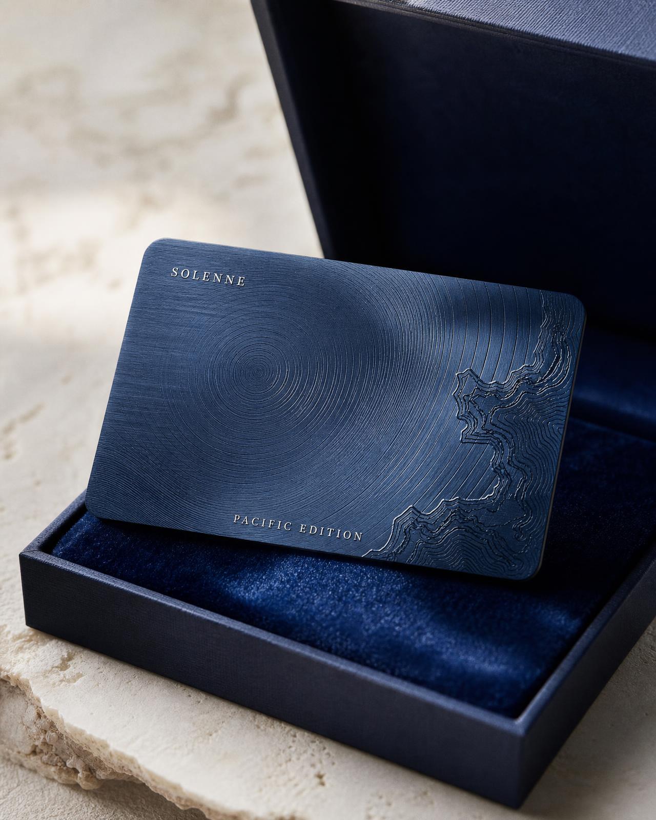Pacific Edition deep blue titanium card with engraved concentric waves, half lifted from a navy box