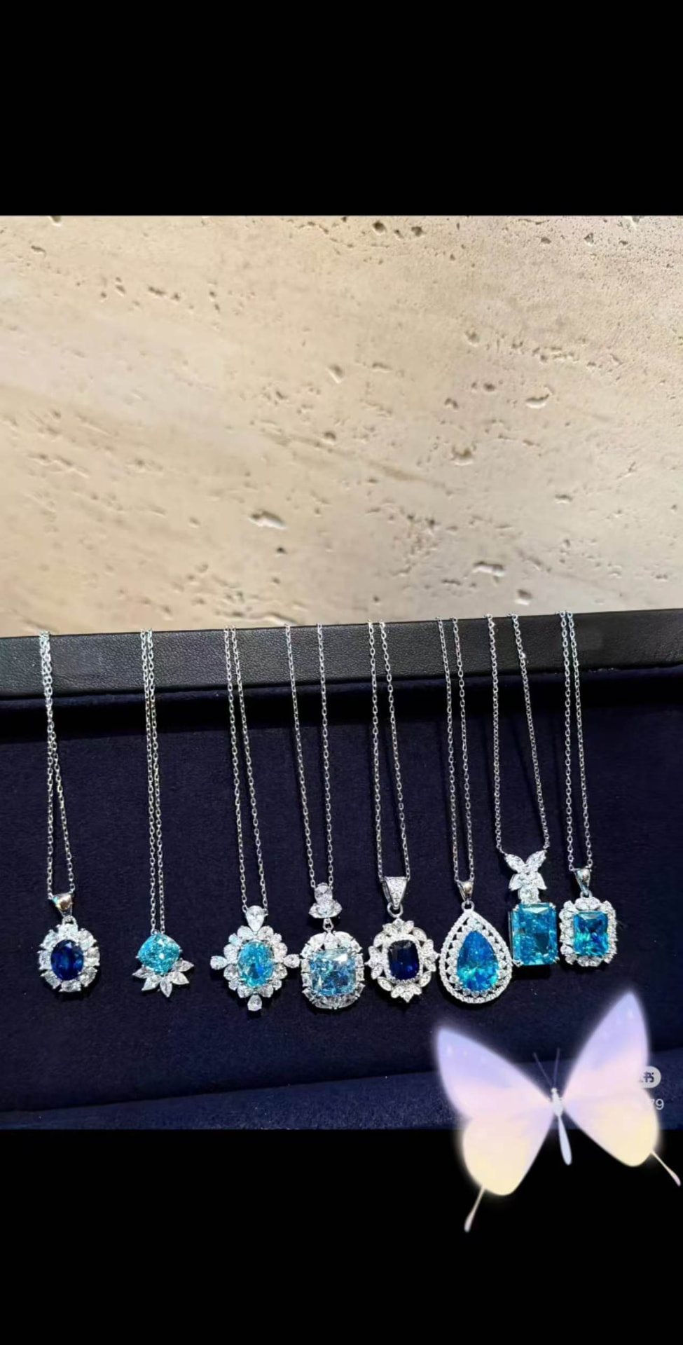 Eight blue gemstone halo pendants displayed on a navy jewellery tray