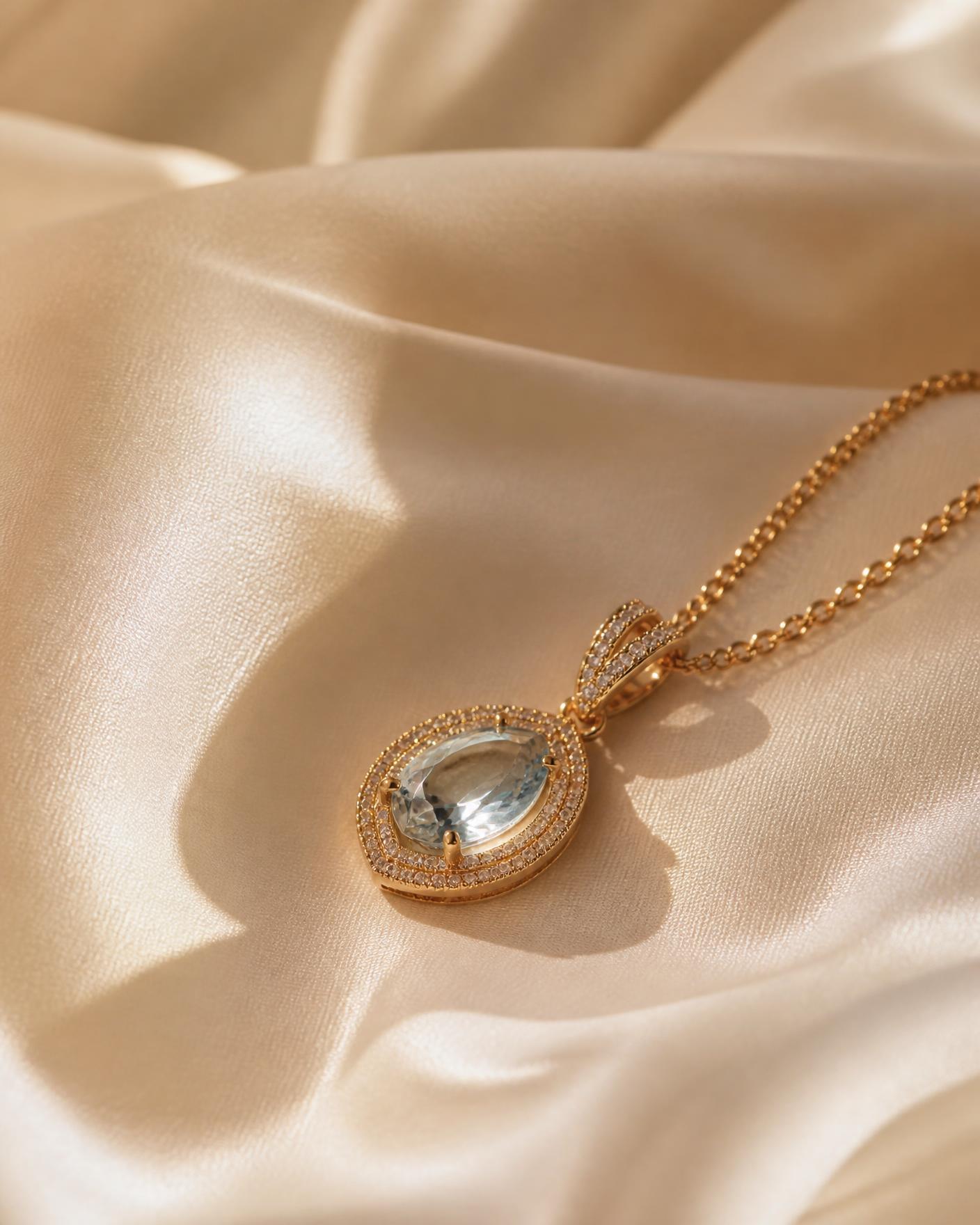 Gold halo pendant with a pale blue gemstone resting on ivory silk